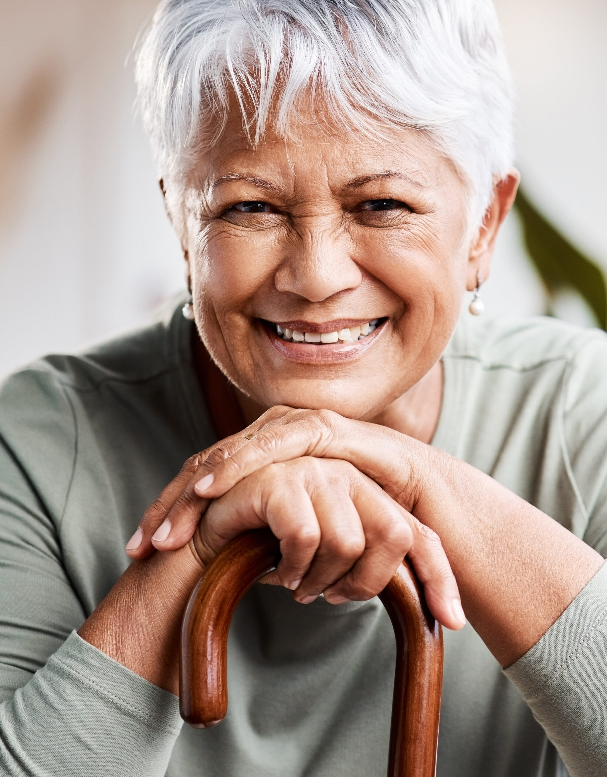 A joyful senior woman rests her hands on a cane, smiling warmly to represent alice.care’s commitment to safe, flexible, and empowering in-home care for older adults.