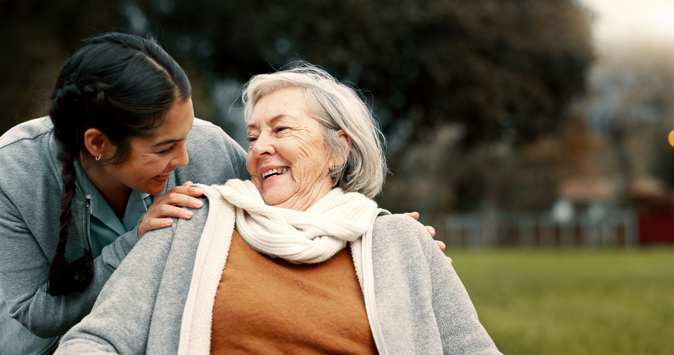 A cheerful caregiver and senior woman share a laugh outdoors, symbolizing the compassion, trust, and joy that define the alice.care experience.