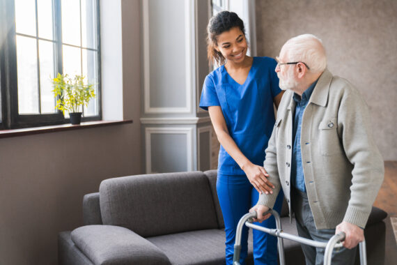 A cheerful caregiver helps an elderly man using a walker, symbolizing the empowerment, flexibility, and fulfillment caregivers experience working with alice.care.