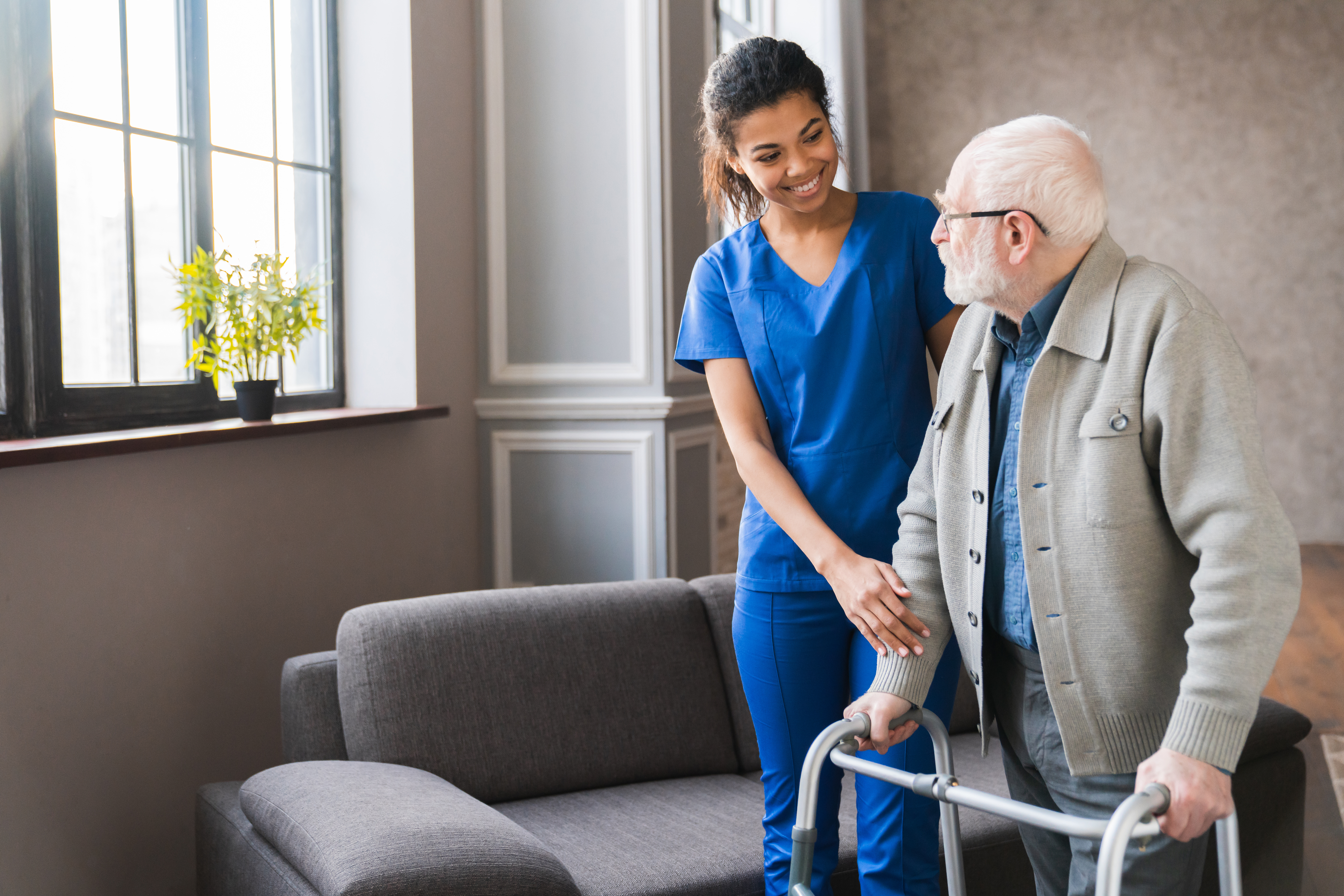 A cheerful caregiver helps an elderly man using a walker, symbolizing the empowerment, flexibility, and fulfillment caregivers experience working with alice.care.