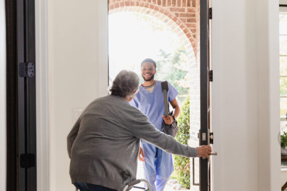 A smiling caregiver arrives at a senior’s home as the client opens the door, symbolizing the ease, responsiveness, and compassion of alice.care’s modern home-based care model.