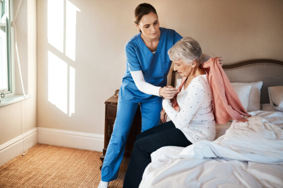 A caregiver assists an elderly woman in putting on a sweater in a softly lit bedroom, highlighting comfort, dignity, and independence in adaptive clothing care.