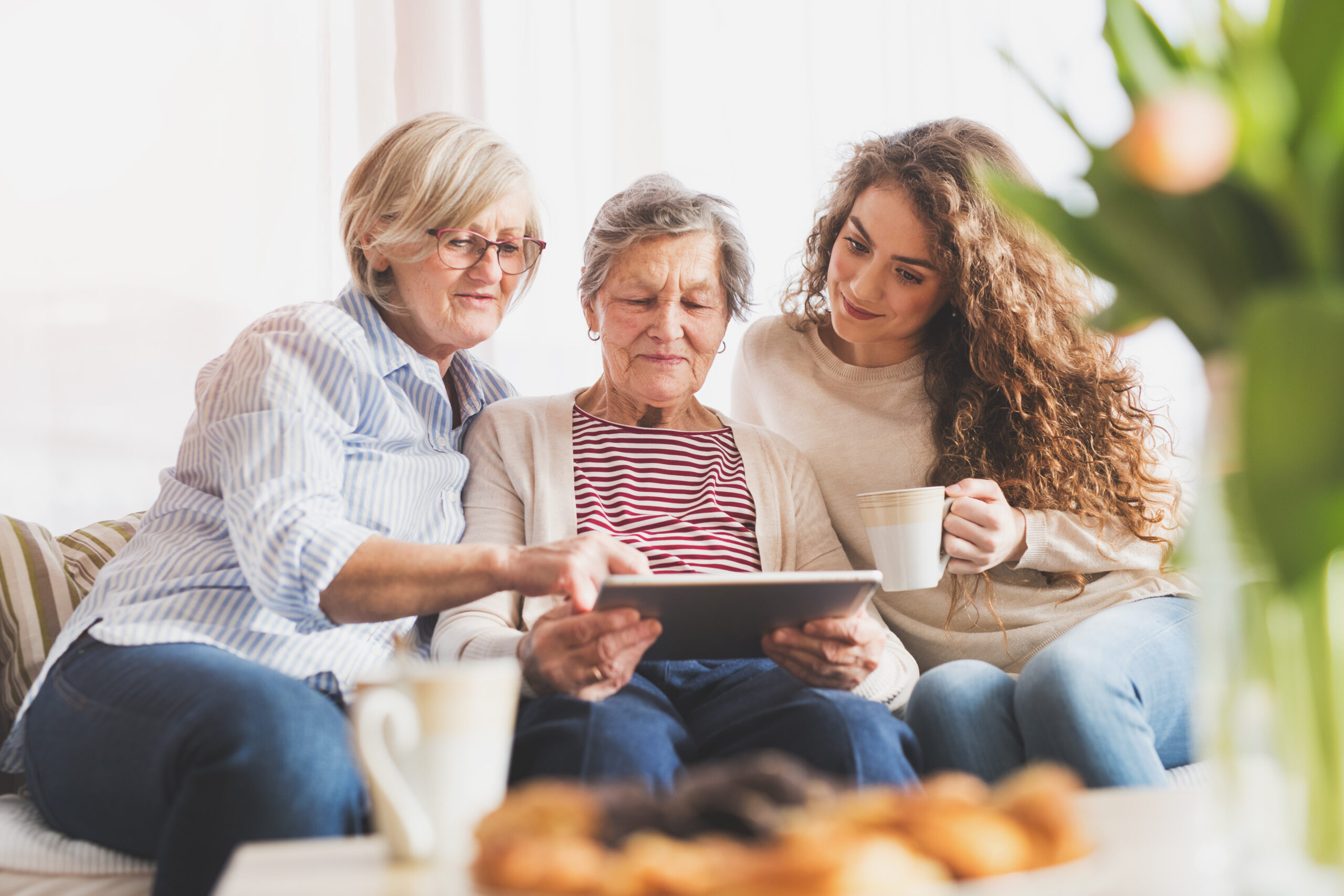 Three generations of women sitting together at home, reviewing information on a tablet and sharing a quiet, supportive moment.