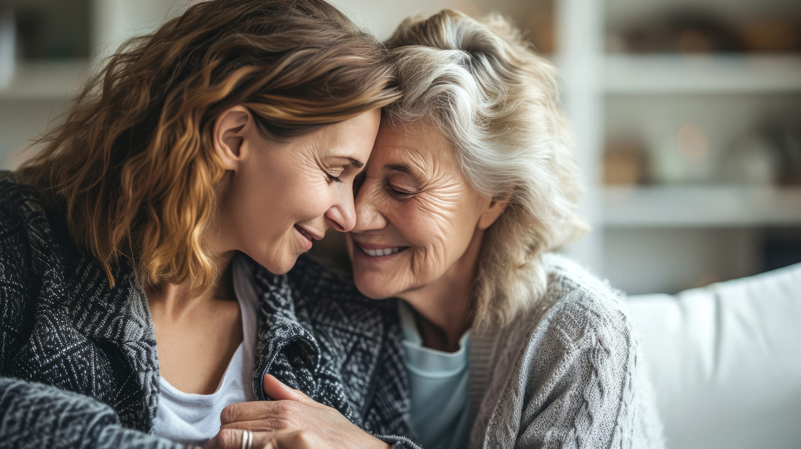 An older mother and her adult daughter laughing together at home, sharing a warm, joyful moment.